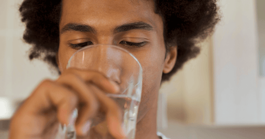 Young man drinking a glass of water, highlighting the importance of hydration for maintaining spinal health and preventing sciatica.